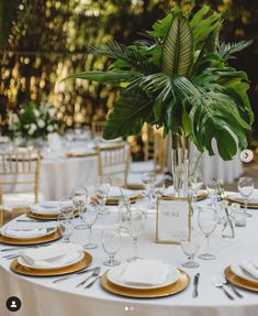 the table is set with white and gold plates, silverware, and greenery