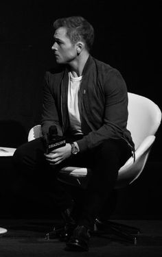 a black and white photo of a man sitting on a chair with a microphone in his hand