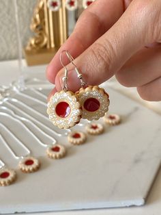 a person is holding onto some small red and white earrings on a table next to cookies