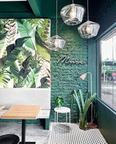 the interior of a restaurant with green brick walls and plants on the tables, along with hanging lights