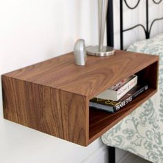 a wooden shelf on the side of a bed next to a night stand with books