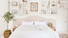 a bed with white linens and pillows in a room filled with bookshelves