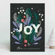 a christmas card with the word joy on it, surrounded by evergreen leaves and berries