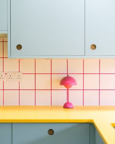 a pink lamp sitting on top of a counter next to a white cabinet and yellow counter