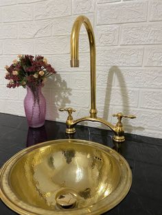 a gold sink sitting on top of a black counter next to a vase with flowers