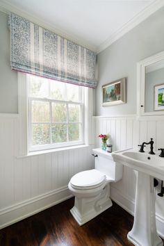 a white toilet sitting next to a sink in a bathroom under a window with valance