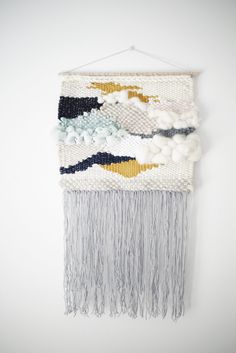 a wall hanging with white, blue and yellow beads on it's sides that have tassels attached to them