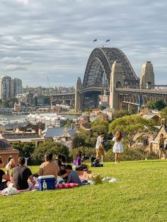 people are sitting on the grass in front of sydney harbour bridge and opera house, australia