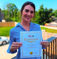 a woman holding up a certificate in front of her face and smiling at the camera