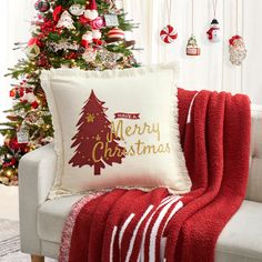 a christmas tree is next to a couch with a red and white throw pillow on it