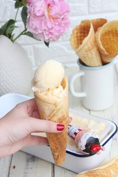 a hand holding an ice cream cone over a container filled with ice cream and pink flowers