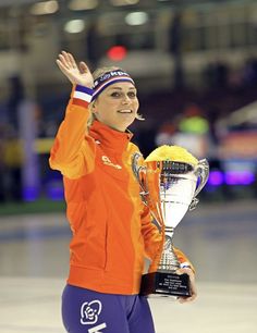 a woman in an orange jacket holding up a trophy and wearing blue leggings