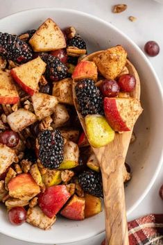 a bowl full of fruit and nuts with a wooden spoon in the bowl next to it