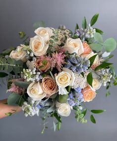 a person holding a bouquet of flowers with greenery on the bottom and blue, white, and pink colors