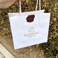 someone holding up a white shopping bag with the word godiva on it