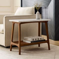 a table with two books on it in front of a couch and a vase filled with flowers