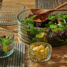 three glass bowls filled with different types of salads and vegetables on top of a wooden table