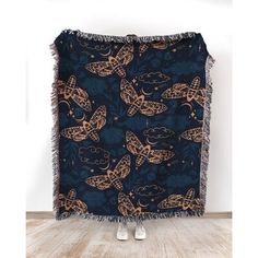 a blue blanket with gold butterflies on it and fringes hanging from the bottom, in front of a white wall