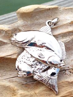 a silver fish charm sitting on top of a piece of wood