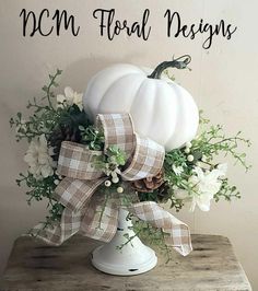 a white pumpkin decorated with flowers and greenery on top of a wooden table next to a sign that says, mom floral designs