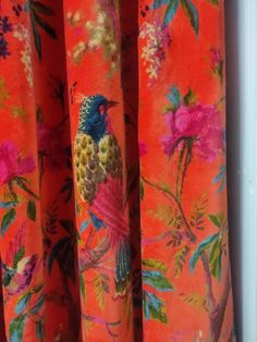 an orange curtain with a colorful bird on it's side and pink flowers in the background