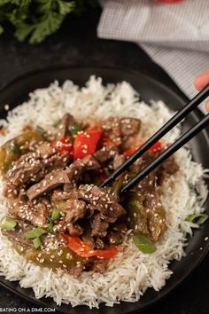 someone is holding chopsticks over some rice with beef and peppers on the side