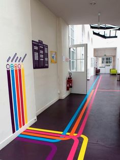 a hallway with colorful lines painted on the floor and white walls, leading to an office building