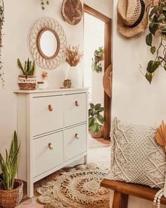 a white dresser sitting next to a mirror and potted plants