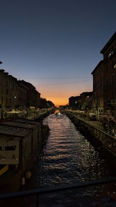 the sun is setting over a canal with buildings on both sides and lights in the distance