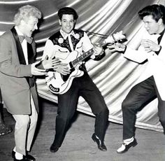 three men in suits and ties are playing guitars