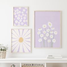 three framed pictures hang on the wall above a white shelf with books and vases