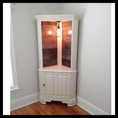 a corner cabinet in the corner of a room with wood floors and white paint on it