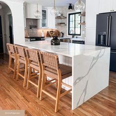 a kitchen with an island and chairs in the center, surrounded by white cabinets and wood floors