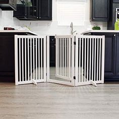 a white dog gate in the middle of a kitchen with black cabinets and wooden floors