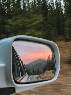 the side view mirror of a car with trees in the back ground and mountains in the background