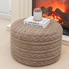 a coffee table sitting next to a fireplace with books on it and a cup in front of the fire