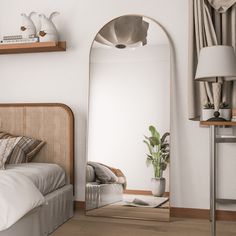 a bedroom with a bed, mirror and plant on the wall next to it's headboard