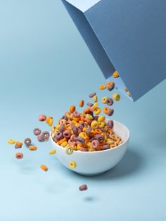 cereal is falling into a bowl on a blue background with an open book in the corner