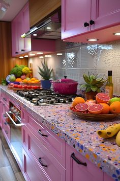 a kitchen with pink cabinets and counter tops filled with fresh fruit, including bananas, grapefruits, oranges, and pineapples