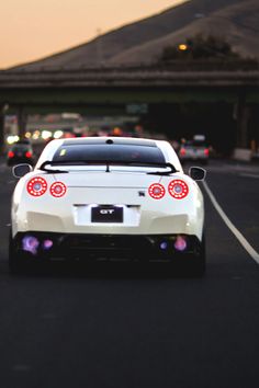 a white sports car driving down a street next to a parking lot with lights on