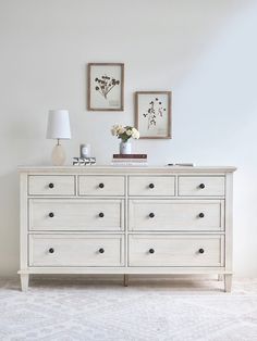 a white dresser with flowers and pictures on the wall