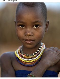 a young boy wearing beaded necklaces and bracelets on his neck, looking at the camera