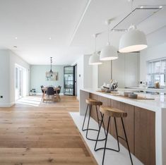 an open kitchen and dining room with white walls, wood flooring and bar stools