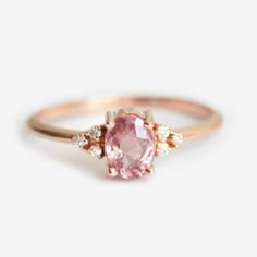 an engagement ring with a pink stone in the center and two diamonds on each side