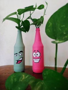 two bottles with faces painted on them sitting next to a plant