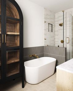 a white bath tub sitting in a bathroom next to a walk in shower and wooden shelves