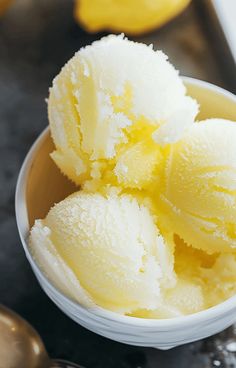 three scoops of ice cream in a bowl on a table with spoons next to it