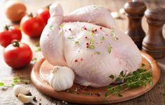 a whole chicken sitting on top of a wooden cutting board next to tomatoes and garlic