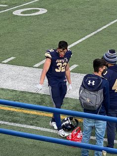 two football players are walking off the field with their backpacks in hand and one is wearing a helmet