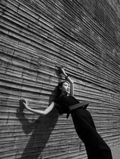 a woman leaning against a brick wall with her hands on the back of her head